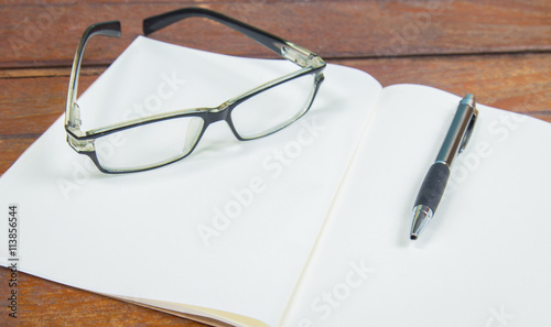 open notebook with pen and glasses on a wooden background
