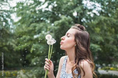 Young girl in a dress blowing dandelion in spring garden. Springtime. Spring allergy 