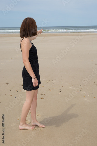 Young brunette woman in summer blackdress standing on beach © OceanProd