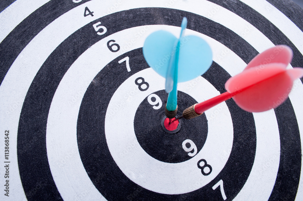 Red and blue dart arrows hitting in the target center of dartboa