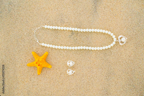 Starfish and pearl necklace on the white sand at the beautiful beach on sunny day.