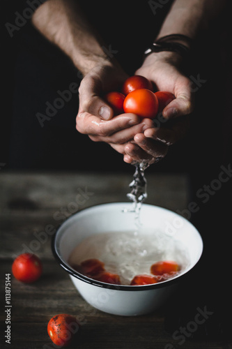 Tomatoes in hands. Man washing freshly picked cherry tomatoes in bowl on rustic wooden table. Selective focus