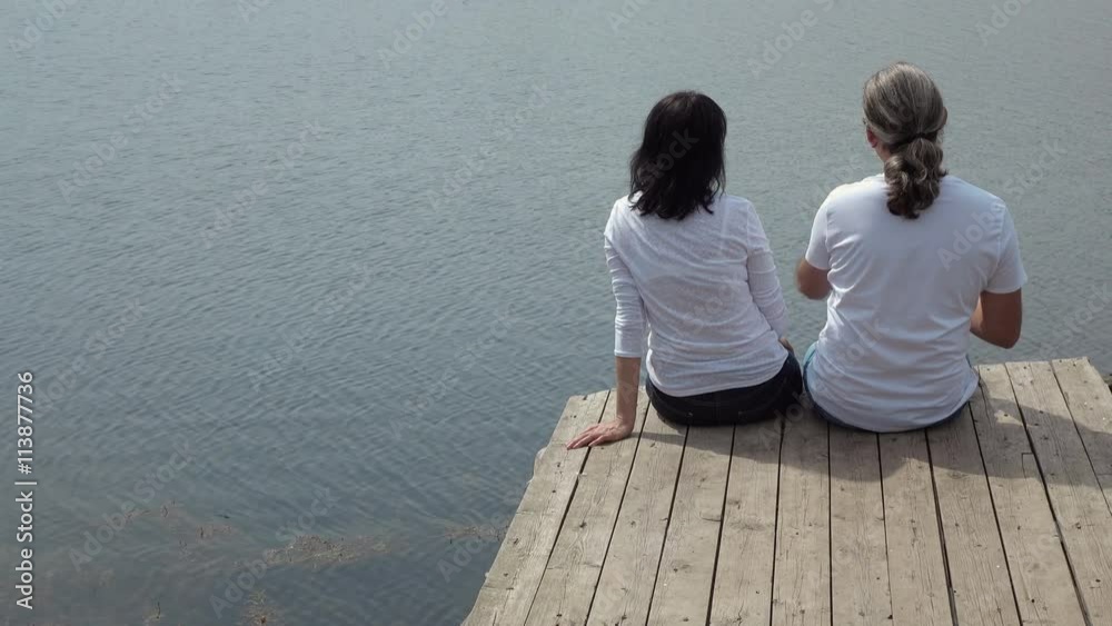 man and woman sitting on the board table looking at the lake. 4K stock footage clip.
