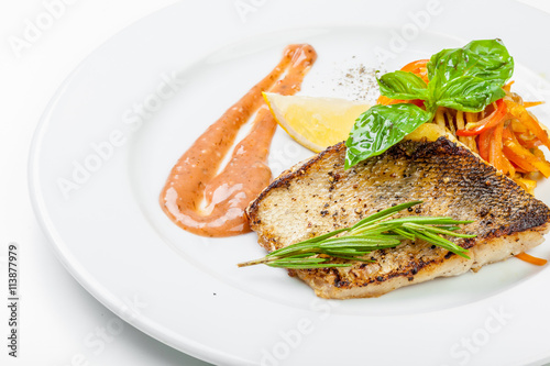 Dish of fish fillet with basil and lemon on plate isolated on white