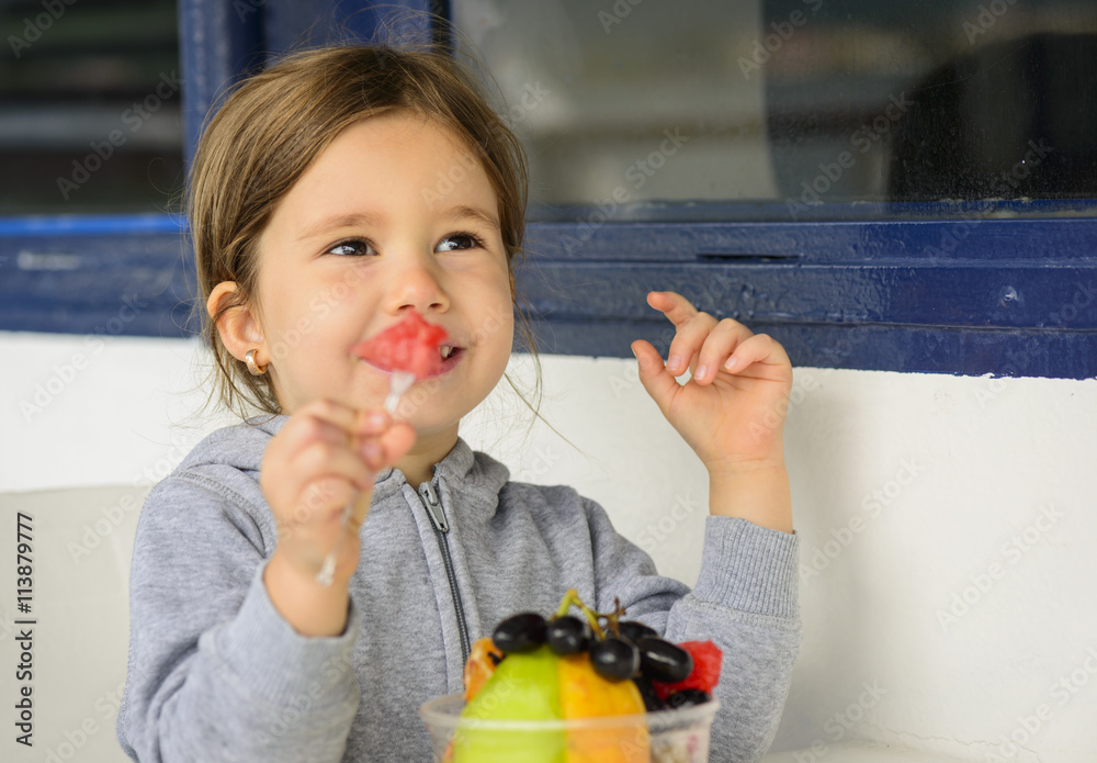 Happy little girl eating fruit salad using fork. Little girl eating healthy snack Stock Photo
