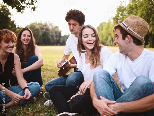 group of friends together in a park having fun and playing music with a guitar © juripozzi