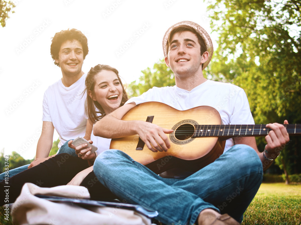 group of friends together in a park having fun and playing music with a guitar group of friends together in a park having fun and playing music with a guitar