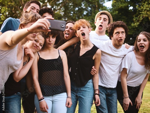 large group of friends together in a park having fun and taking a selfie with smartphone