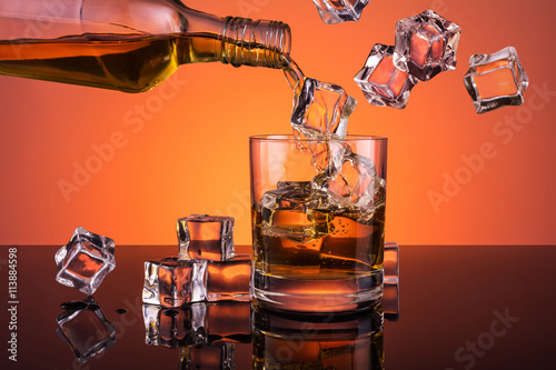 Whiskey pouring from bottle into glass full of ice