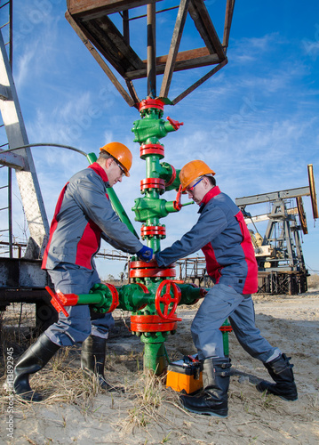 Workers in the oilfield repairing wellhead with the wrench. Pumpjack and wellhead background. Oil and gas concept. 