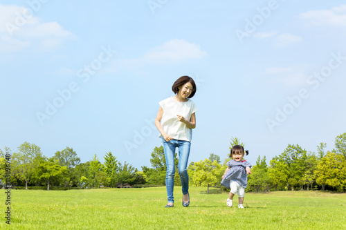 青空の下、芝生の公園で幼い女の子とt走る母子