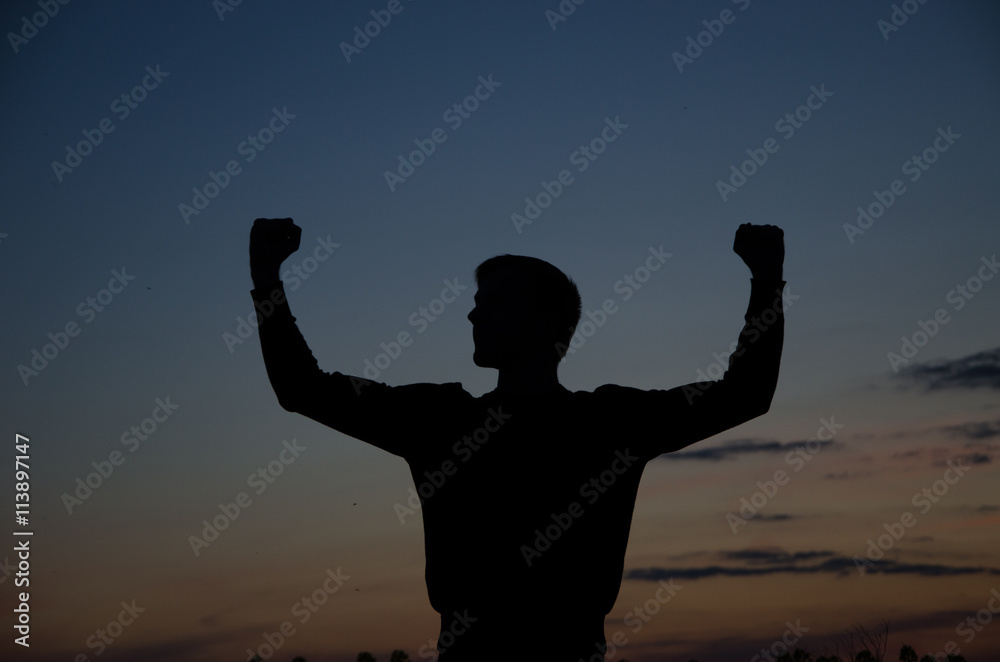 Silhouette of a strong fighter. Confident young fitness man with strong hands and clenched fists. Dramatic light