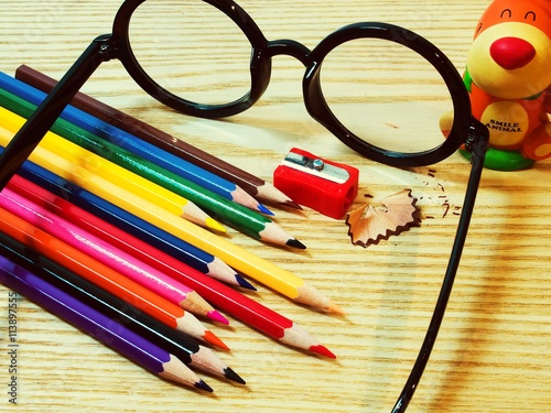 A dozen of color pencil on wood texture with sharpener and glasses