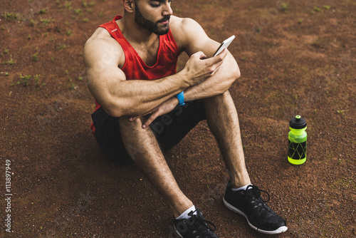 Athlete outdoors sitting on ground looking at cell phone