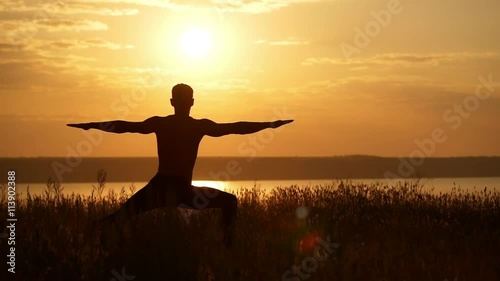Silhouette of young sportive man practicing yoga at sunset. Slow motion.