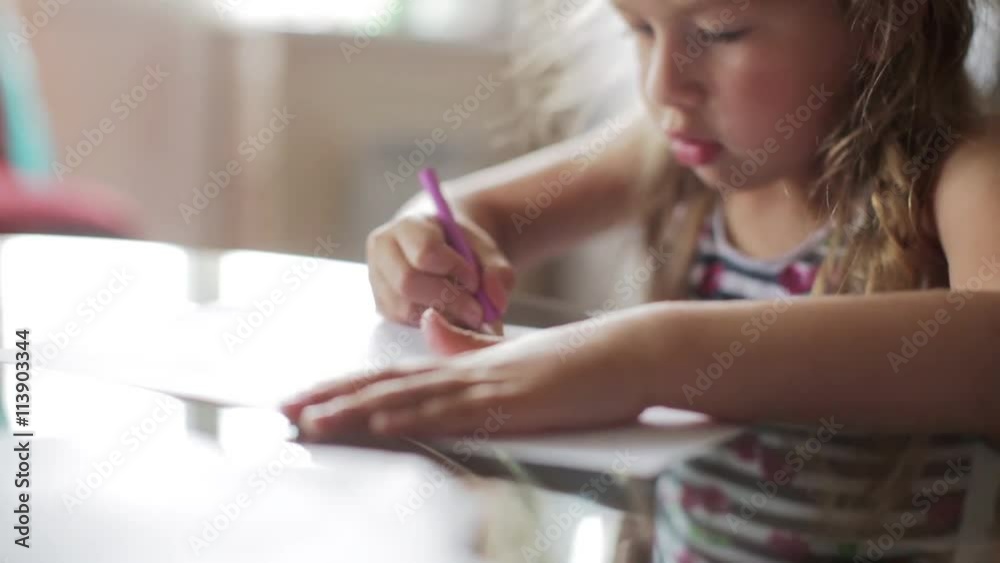 little girl draws with crayons sitting at table. close up