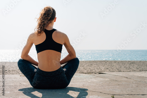 Athletic girl with curly hair in a sports bra sitting on a beach photo