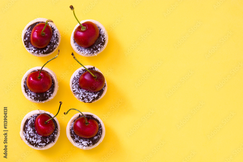 Delicious chocolate tartlets with one cherry, chocolate and coconut on yellow background

