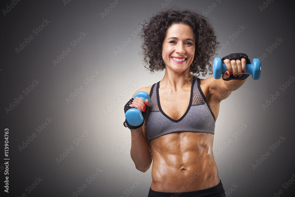 Fit woman training with dumbbells on grey bakground Fit woman training with dumbbells on grey bakground