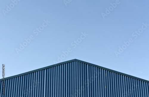 Blue modern warehouse roof against blue sky.