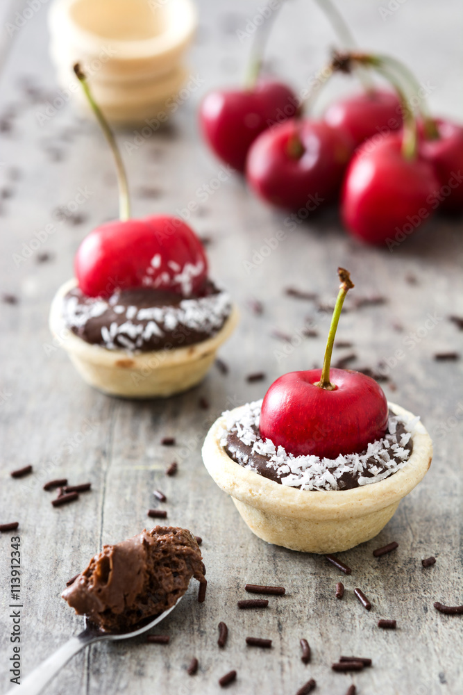 Delicious chocolate tartlets with one cherry and coconut on a wooden table


