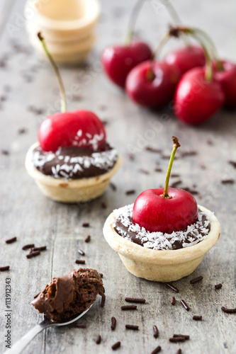 Delicious chocolate tartlets with one cherry and coconut on a wooden table