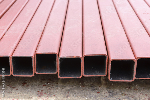 The square tube,the square tube in the construction site.The pile of the red square tube on the floor after painting process.The red square tube for rusty protection.Closeup of square tube profile.