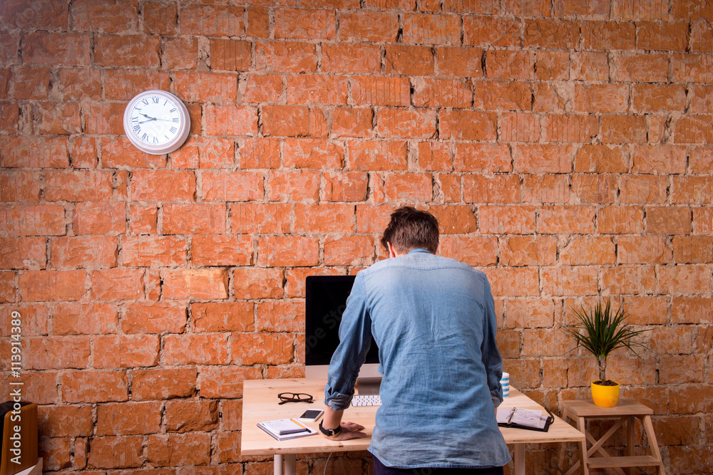 Sad businessman standing at office desk, rear view