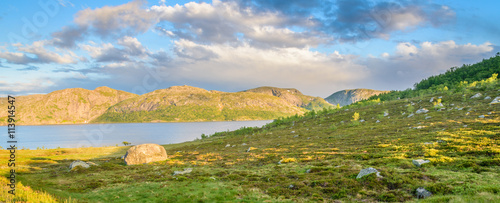 Panorama of a rocky hill at sunset in a Norwegian mountain, with a lake in the background