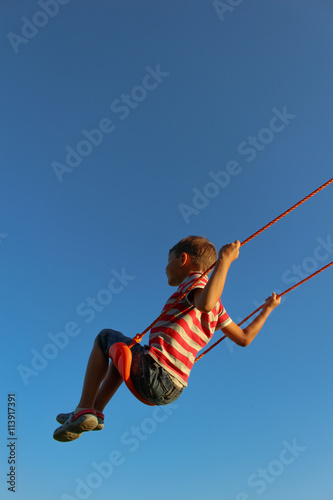Little boy on a swing against blue sky. Background with copy space © vejaa