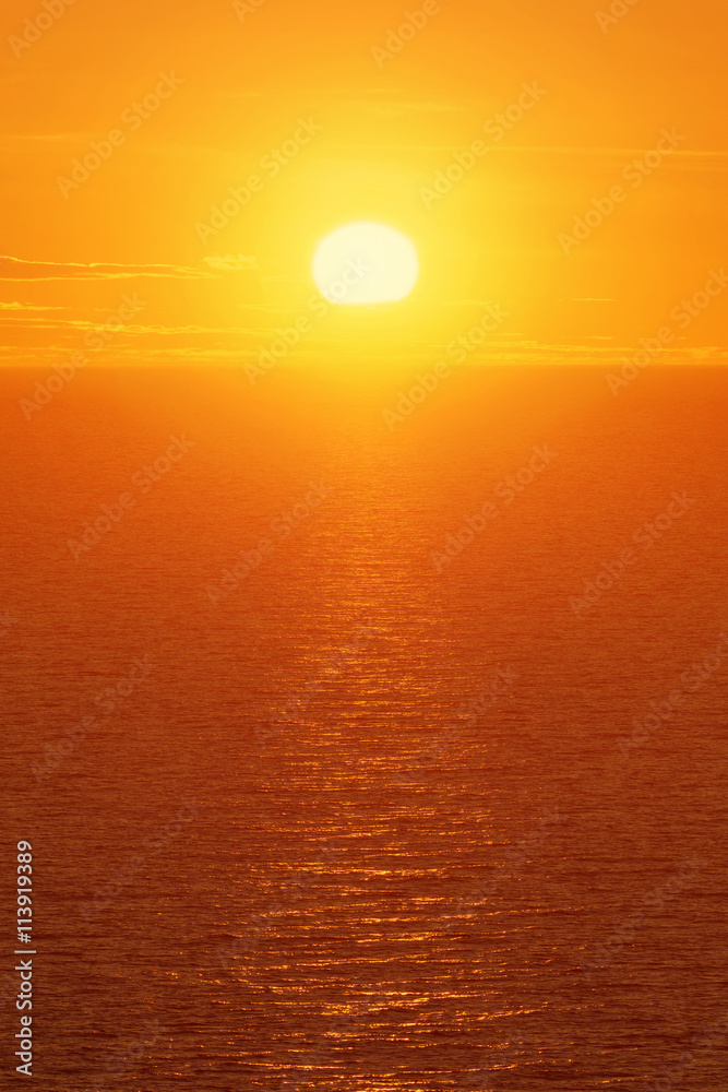 Warm orange sun over open ocean with ripples and light clouds in