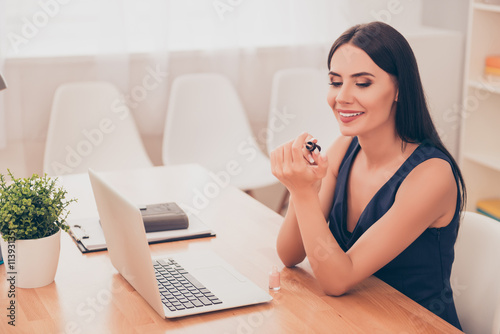 Smiling pretty secretary sitting with laptop and doing manicure