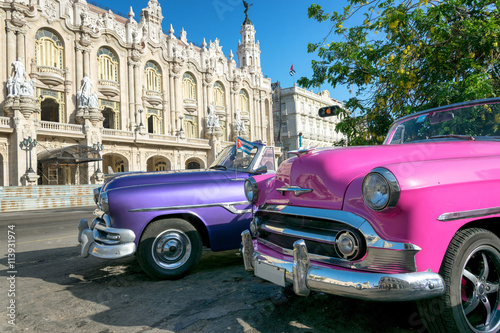 Two colorful vintage taxis and the Great Theater on the background in Havana, Cuba