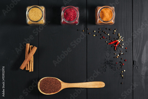 Ground spices in bottles with spon, papper, cinnamon on black wooden background. Top view. Free space.