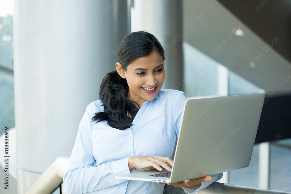 Closeup portrait, young pretty woman in blue shirt resting hands on keyboard, browsing digital computer laptop, isolated indoors office interior background Closeup portrait, young pretty woman in blue shirt resting hands on keyboard, browsing digital computer laptop, isolated indoors office interior background
