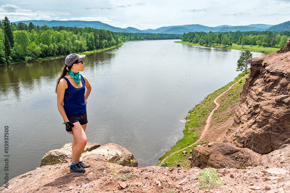 girl stands on hill above the river