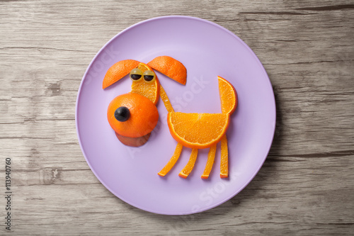 Dog made of juicy orange on plate and board