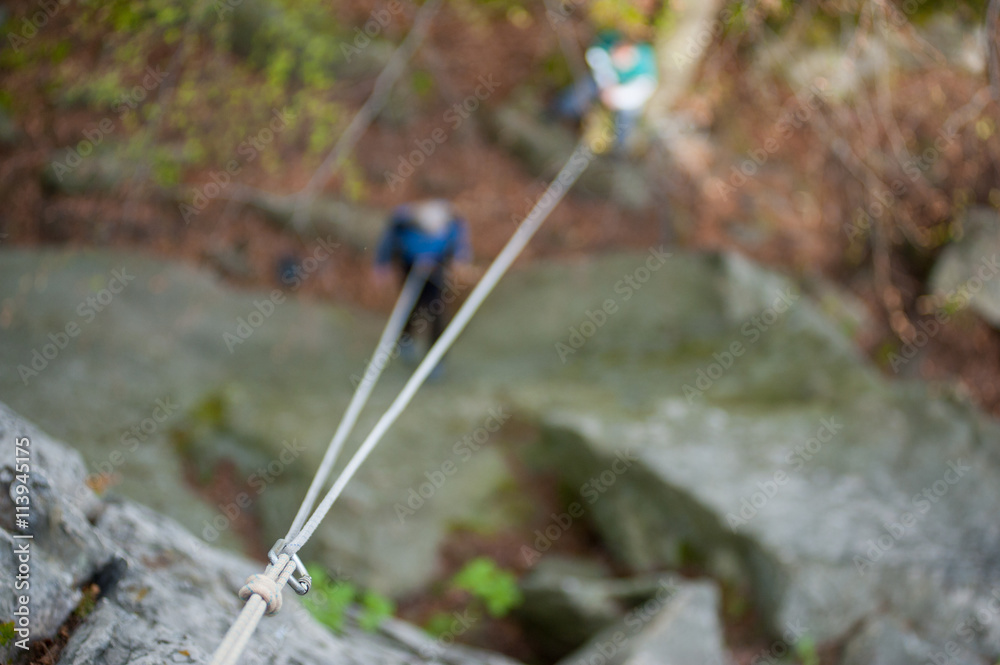 Hanging of climbers carabiner and rope on the rock on blurred background people at the ground. Security climb concept
