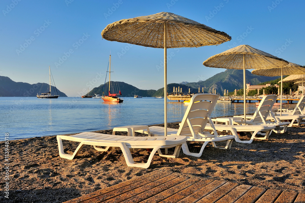 Beach with sunshades and sunbeds against the backdrop of the picturesque bay of blue sea and mountains