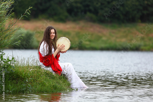 Young brunette woman playing tambourine at a lake