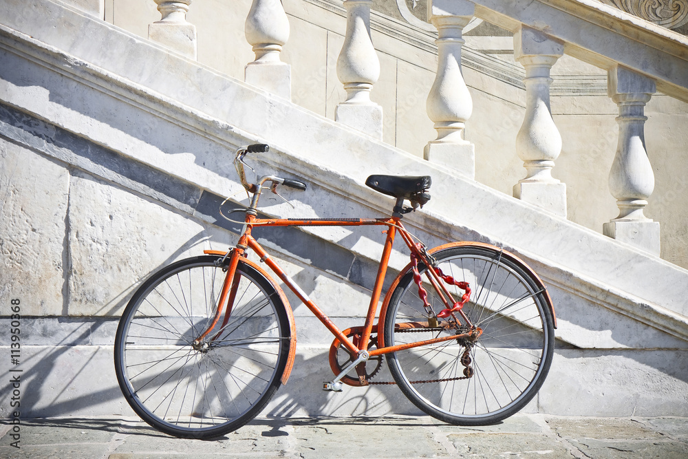 Orange old bicycle against a marble wall (Tuscany - Italy)