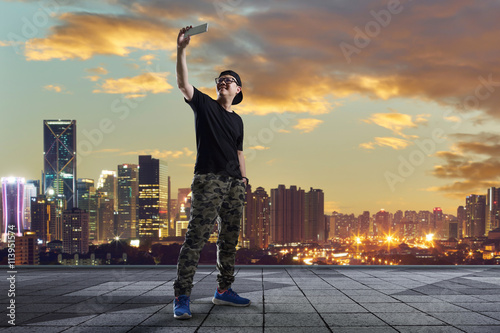 man taking selfie at rooftop on city skyline background