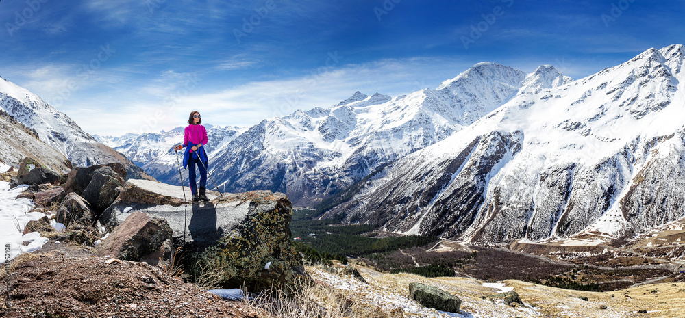 Hiker woman walking on mountain trail with hiking sticks, looking at view in Elbrus region, Caucasus mountains