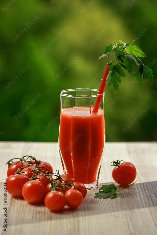 A glass of tomato juice, lying next to a branch of tomatoes A glass of tomato juice, lying next to a branch of tomatoes