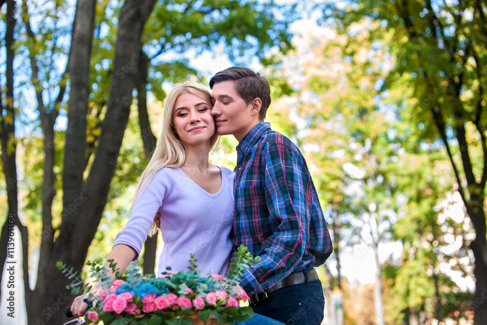 Young beautiful couple with flowers basket on retro bike kissing in summer park . Date of loving couple in outdoor park. Young beautiful couple with flowers basket on retro bike kissing in summer park . Date of loving couple in outdoor park.