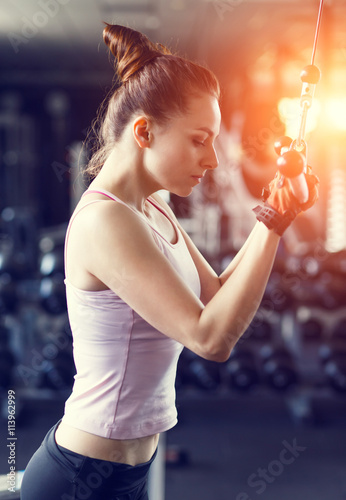 Young woman doing pushdown on cable machine in gym photo