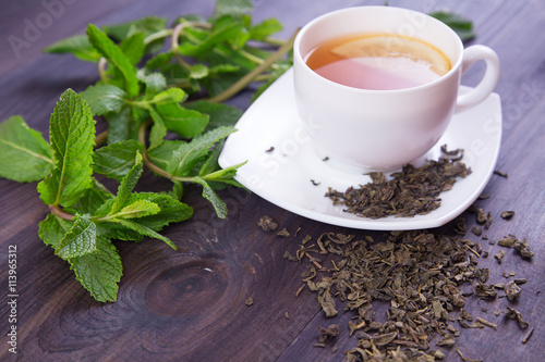 Cup of green tea with lemon and mint leaves on a dark wooden background