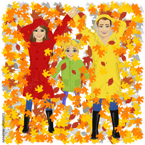 young happy family of daughter mother and father lying on autumn leaves in park