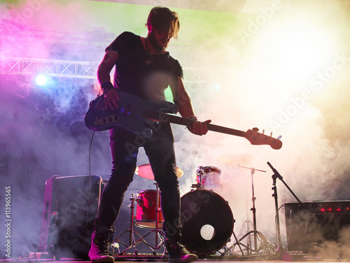 Rock band performs on stage. Bassist in the foreground.