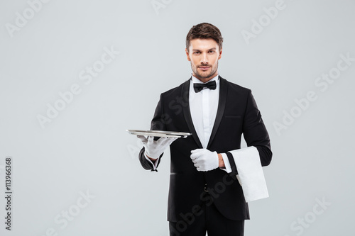 Attractive butler in tuxedo standing and holding silver empty tray photo